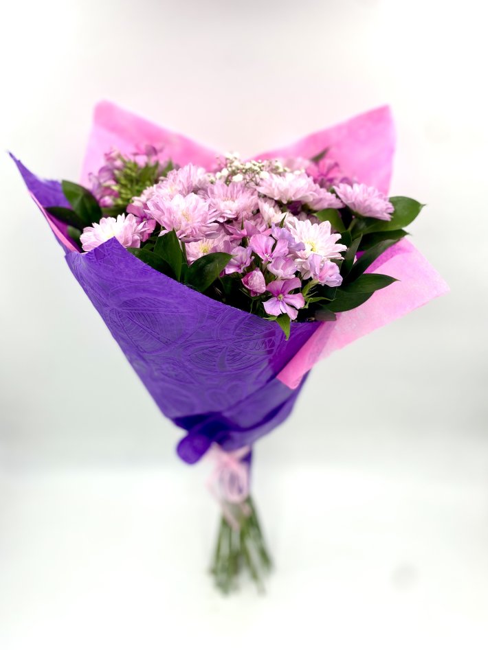 זר פרחים ורודים עדינים עטוף בנייר סגול ורוד, עם עלים ירוקים להשלמת המראה האלגנטי