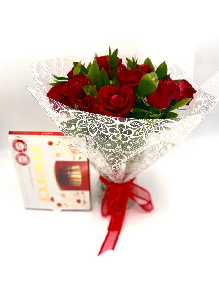 זר ורדים אדומים יוקרתי עטוף בנייר לבן עם עיטורים עדינים, מלווה בקופסת שוקולד Merci. מושלם למתנה רומנטית